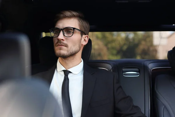 Pensativo empresario confiado en traje completo con gafas mirando hacia otro lado mientras está sentado en el coche . —  Fotos de Stock