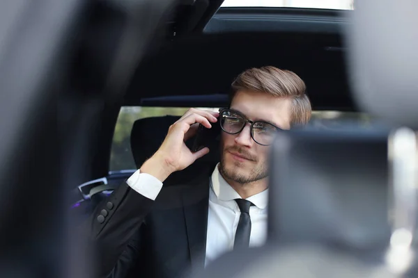 Doordachte zelfverzekerde zakenman die aan de telefoon praat terwijl hij in de auto zit. — Stockfoto