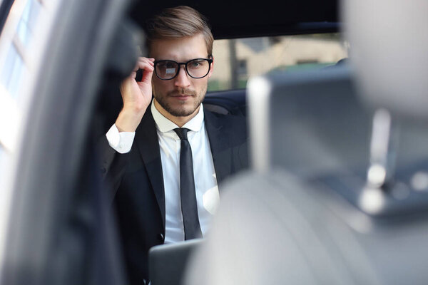 Задумчивый уверенный бизнесмен держит руку на стекле, сидя в роскошной машине
.
