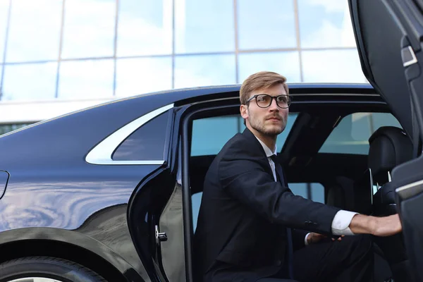 Knappe serieuze jonge zakenman die in zijn comfortabele nieuwe auto zit en naar het kantoor gaat. — Stockfoto