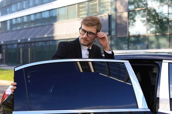 Elegantní mladý obchodník vstupující do auta, když stojí venku. — Stock fotografie