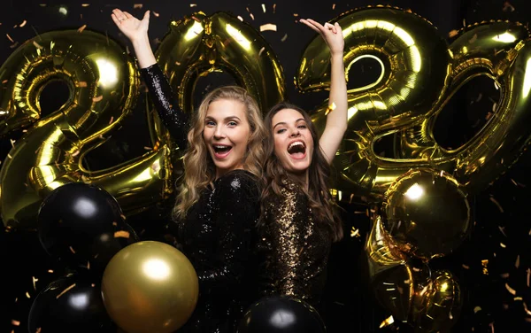 Meninas lindas felizes em vestidos de festa sexy elegantes segurando balões de ouro 2020, se divertindo na festa de Ano Novo . — Fotografia de Stock