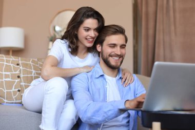 Mutlu çift oturuyor, oturma odasında dinleniyor, birlikte online alışveriş yapmak için dizüstü bilgisayar kullanıyorlar, film izliyorlar.