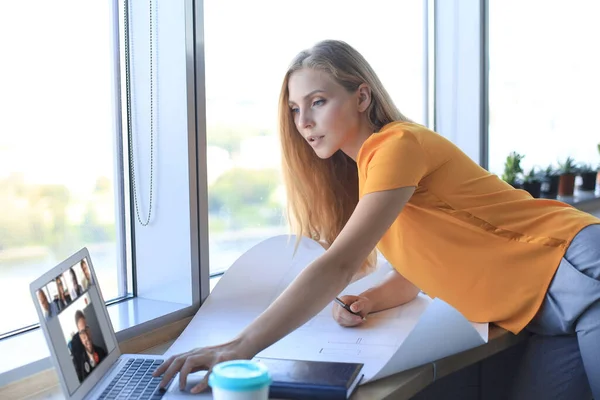 Mulher moderna bonita está escrevendo algo no modelo e usando laptop enquanto trabalhava no escritório criativo — Fotografia de Stock
