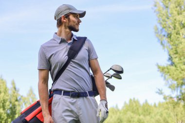 Golf oyuncusu yaz golfü sırasında yolda yürüyor ve çanta taşıyor.