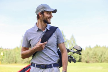 Golf oyuncusu yaz golfü sırasında yolda yürüyor ve çanta taşıyor.