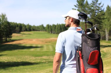Golf oyuncusu yaz golfü sırasında yolda yürüyor ve çanta taşıyor.