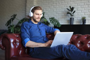 Kulaklık takan mutlu genç adam kendini tecrit sırasında bilgisayarla evden çalışıyor.