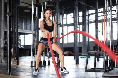 Formda bir kadın spor salonunda antrenman yaparken halat kullanıyor.