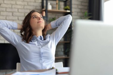 Genç bir kadın ellerini kafasının arkasında çapraz yaptı, evde tatilin tadını çıkarıyordu. Huzurlu kaygısız iş kadını bilgisayarla masada dinleniyor, yan bakıyor, geleceği hayal ediyor.