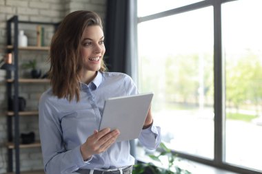 Ev ofisinde tablet üzerinde çalışan çekici, gülümseyen bir kadın.