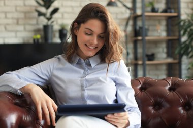 Kanepede tabletli gülümseyen genç kadın.