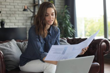 Gülümseyen kız kanepede oturup dizüstü bilgisayarda webinar izliyor. Mutlu genç kadın çevrimiçi uzak kurslarda okuyor.