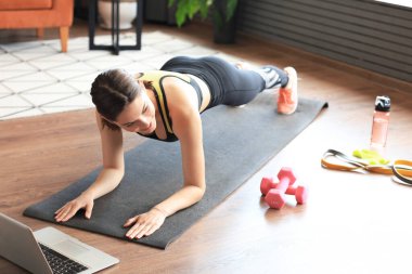 Spor salonundaki kadın dizüstü bilgisayarda kalas yapıyor ve online dersler izliyor oturma odasında eğitim görüyor. Ev aktivitelerinde kal. Üst görünüm