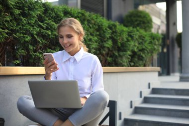 Ofisin yakınında telefon ve dizüstü bilgisayarla çalışan mutlu bir girişimci.