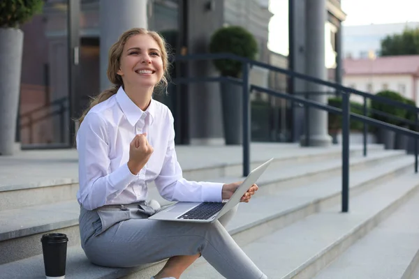 Excited cheerful business woman achieves its goals working with laptop outdoor