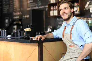 Kafe sahibi. Mutlu adam tezgahın yanında oturuyor, gülümsüyor.