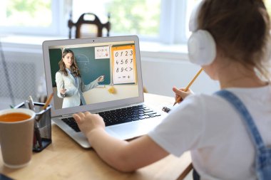 Mesafe öğrenme. Kulaklıklı neşeli küçük kız bilgisayarını kullanarak internetten e-öğrenim sistemini inceliyor..