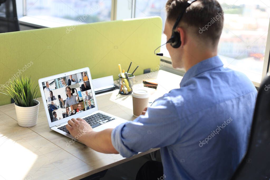 Businessman in headphones talking to her colleagues in video conference. Multiethnic business team working from home using laptop, discussing financial report of their company.