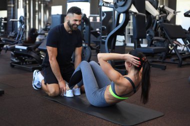 Spor salonunda genç bir bayana karın egzersizi yaptıran antrenör.