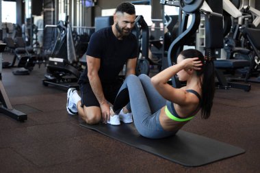Spor salonunda genç bir bayana karın egzersizi yaptıran antrenör.