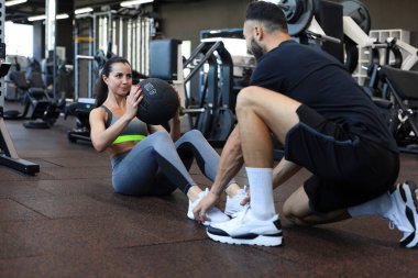 Spor salonunda genç bir bayana karın egzersizi yaptıran antrenör.