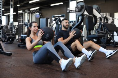 Güzel genç spor çifti jimnastik salonunda sağlık topuyla antrenman yapıyor.
