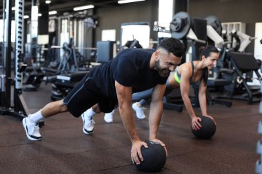 Güzel genç spor çifti jimnastik salonunda sağlık topuyla antrenman yapıyor.