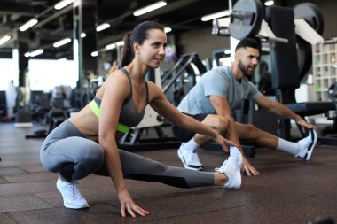 Formda olan iki insan spor salonunda esneme egzersizleri yapıyor.