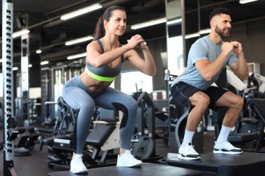 Uygun spor salonunda çömelme hareketleri yapan zinde bir çift.