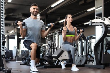 Çekici sporcular spor salonunda dambıllarla çalışıyor.
