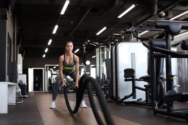 Formda bir kadın spor salonunda antrenman yaparken halat kullanıyor.
