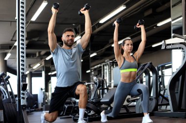 Çekici sporcular spor salonunda dambıllarla çalışıyor.