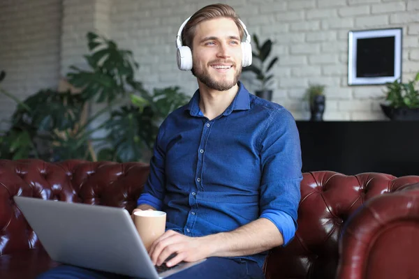 Gelukkige jongeman in koptelefoon werken op laptop van thuis uit tijdens zelfisolatie. — Stockfoto