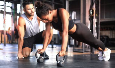 Sportif bir kadın spor salonunda şınav çekiyor, erkek arkadaşı onu izliyor.