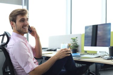 Modern iş adamı ofiste otururken telefonla konuşuyor.