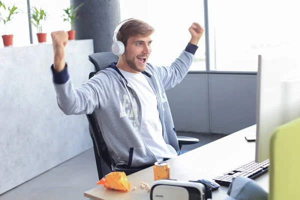 Portrait of ecstatic gamer guy in headphones screaming and rejoicing while playing video games on computer