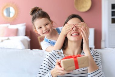 Küçük kız heyecanlı ebeveyne doğum günü hediyesi veriyor, gülümseyen küçük çocuk tebrik ediyor mutlu anneye ve kapalı annenin gözlerine hediye kutusu veriyor.