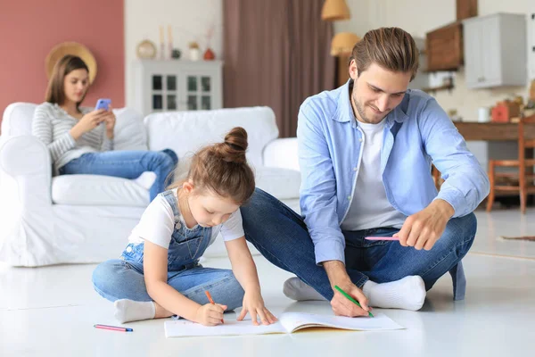 stock image Happy father smilling daughter lying on warm floor enjoying creative activity, drawing pencils coloring pictures in albums, mother resting on couch, family spend free time together