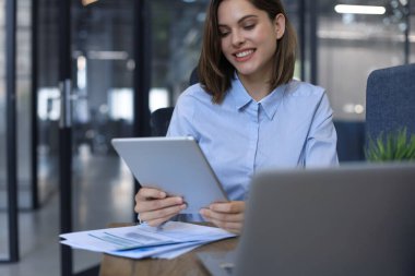 Modern ofiste tablet üzerinde çalışan çekici, gülümseyen bir kadın.