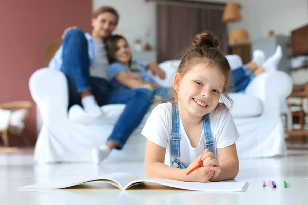 Smiling happy family sit relax on couch in living room watch little daughter drawing in album with colorful pencils. Happy weekends at home