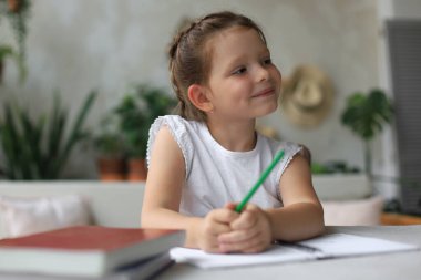 Little girl sit at desk, writing in notebook, do exercises at home, small child handwrite prepare homework clipart
