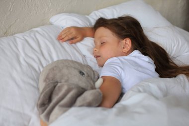 Sevimli küçük kız, oyuncak bir fille yatakta uyuyor.