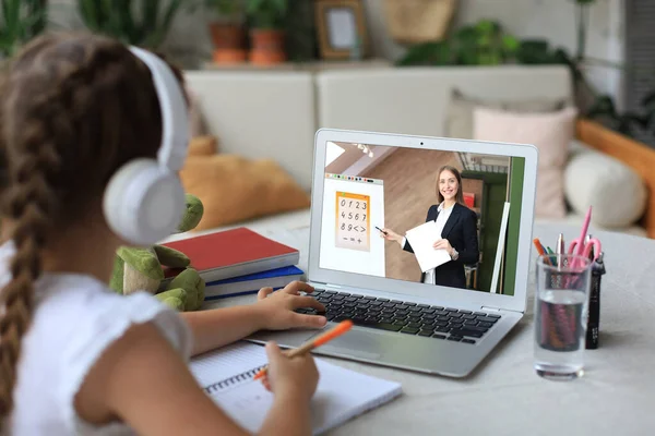 Distance learning. Cheerful little girl girl in headphones using laptop studying through online e-learning system