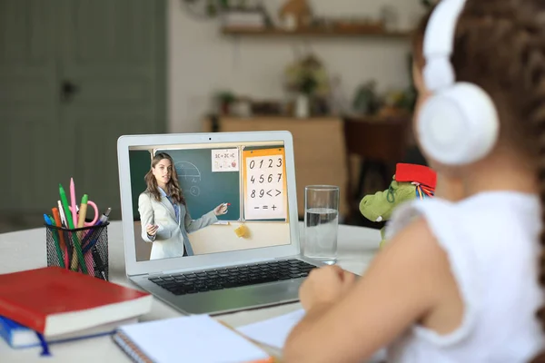 Distance learning. Cheerful little girl girl in headphones using laptop studying through online e-learning system