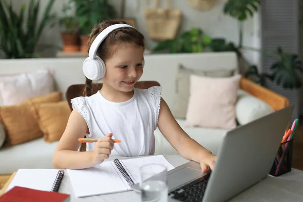 Distance learning. Cheerful little girl girl in headphones using laptop studying through online e-learning system