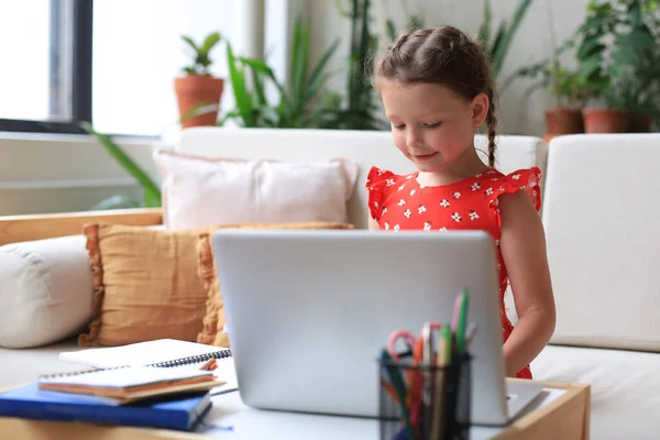 Distance learning. Cheerful little girl using laptop computer studying through online e-learning system