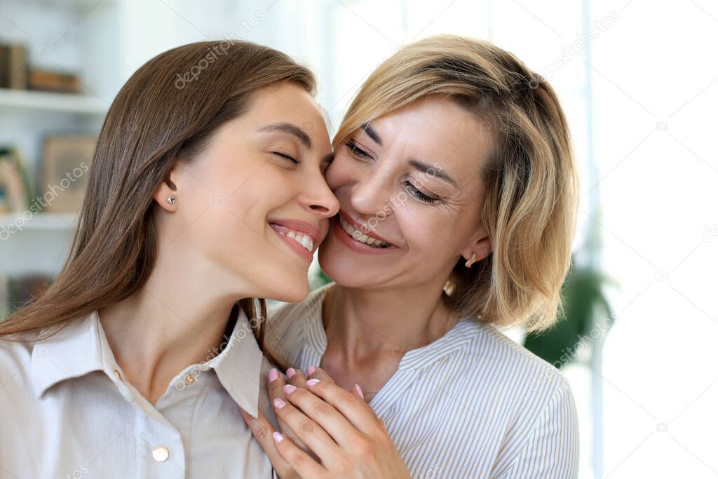 Happy middle aged mother and daughter talking on sofa in living room