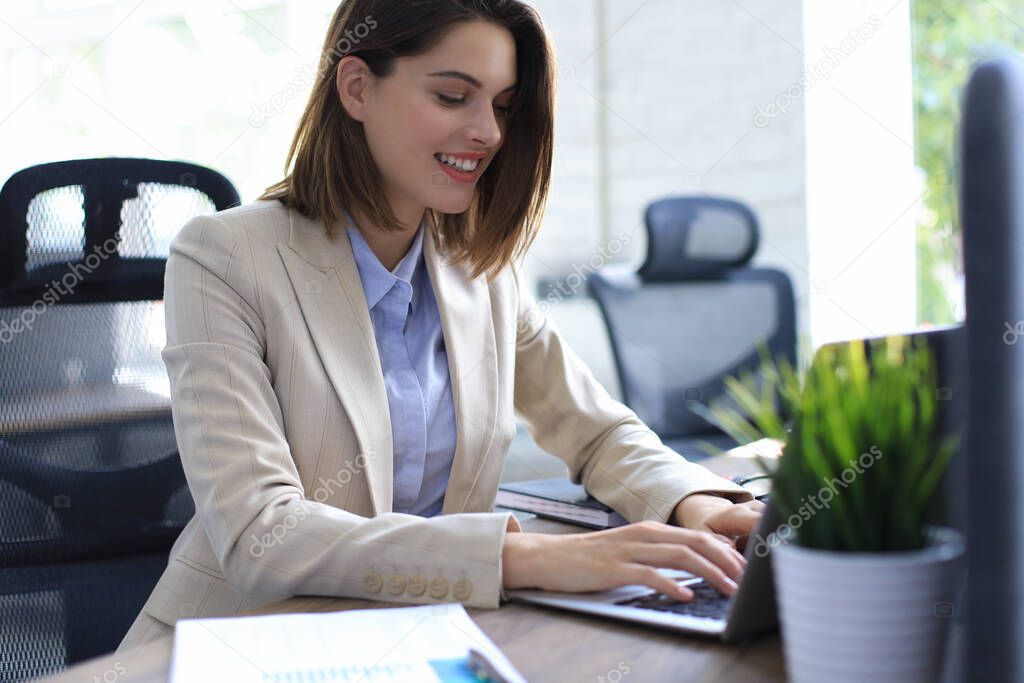 Smiling pretty woman sitting at table, looking at laptop screen. Happy entrepreneur reading message email with good news, chatting with clients online