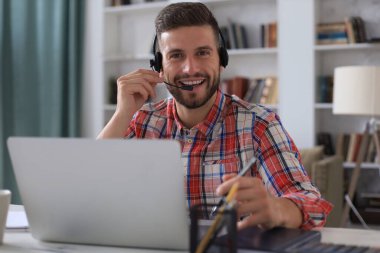 Gülümseyen genç iş adamı ev ofisinden video görüşmesi yapıyor.